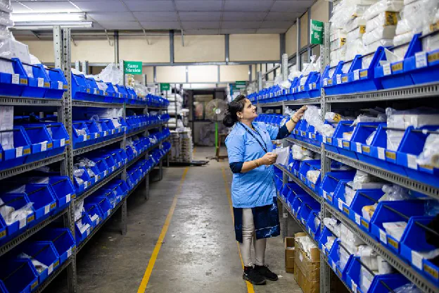 supplier quotation - A worker in a warehouse organizing inventory on shelves with blue bins.