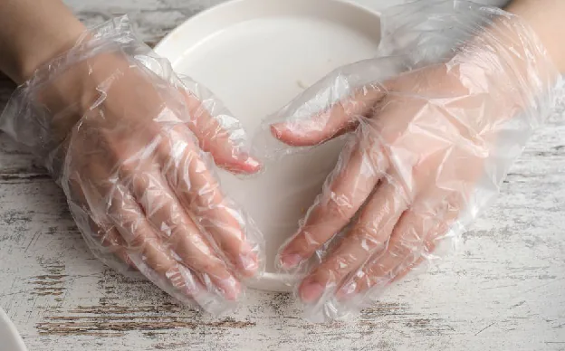 food contact materials - Close-up of hands in plastic gloves holding a plate on a wooden surface.