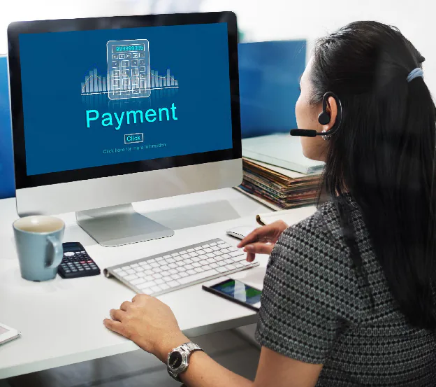 Alt text: Professional reviewing digital payment processing on a desktop computer, analyzing transaction data within a procure-to-pay system while working at a desk with financial tools and documents.