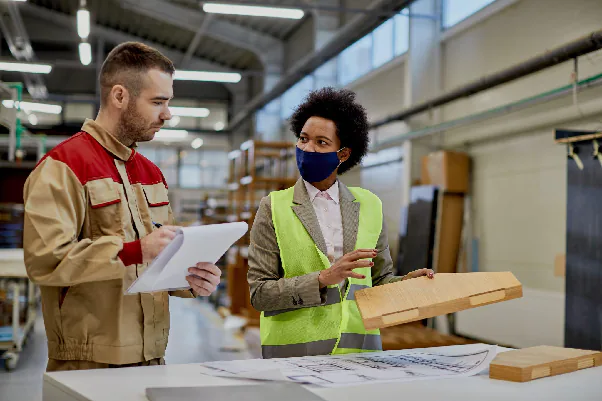 A quality inspector reviews a product sample and paperwork with a factory worker during an on-site supplier verification audit.