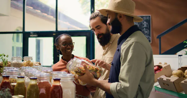 Buyers review a packaged-food jar and discuss its ingredients and labeling with a food supplier as part of supplier verification.